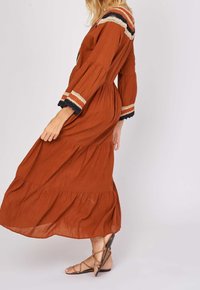 Rust-colored maxi dress in lightweight fabric with tiered design. Features embroidered accents in cream, red, and blue on sleeves and neckline.