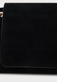 Fekete velúr clutch táska sima textúrával, amely hajtott dizájnnal és látható varrással rendelkezik. Arany színű kiegészítők díszítik az oldalát.