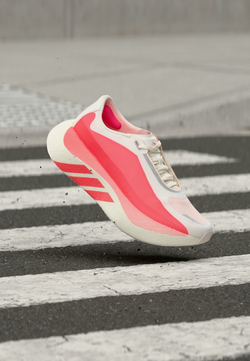 Chaussure de sport blanche et rose flottant au-dessus d'un passage piéton sur une route asphaltée, avec des particules de saleté soulevées du sol.