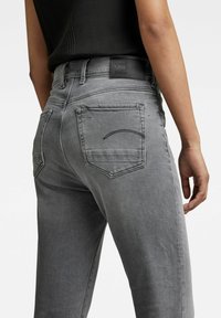 Los jeans de denim gris presentan una silueta ajustada, dos bolsillos traseros con costura curva y una etiqueta de cuero negra en la cintura.