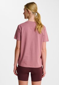 Kortærmet, afslappet t-shirt i støvet rosa bomuld, med rund hals og glat tekstur, parret med mørkeburgunder shorts.