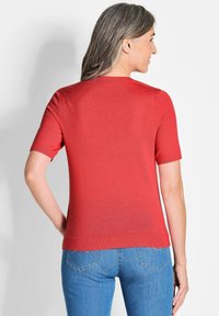 Rode korte mouwen trui met een getailleerd ontwerp en ronde hals. Gladde textuur met geribbelde randen, gecombineerd met blauwe denim jeans.