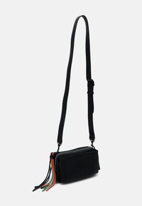 Schwarze Umhängetasche in rechteckiger Form, aus strukturiertem Stoff. Verfügt über einen Reißverschluss und farbenfrohe Quasten in Rot, Grün und Schwarz.