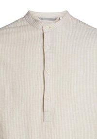 Camicia button-up beige chiaro con colletto alla cinese, caratterizzata da sottili righe verticali e un logo ricamato discreto sul petto.
