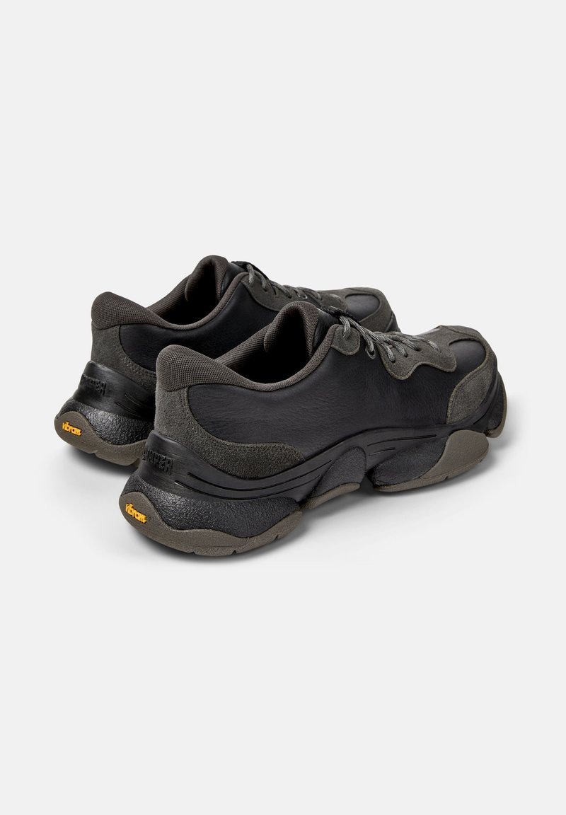 Ein Paar schwarze und dunkelgraue Leder-Sneaker mit strukturierten Sohlen und Schnürdesign, von hinten und seitlich auf weißem Hintergrund gezeigt.
