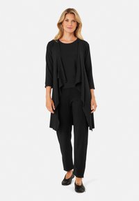 Completo nero a tre pezzi composto da un cardigan fluido, una maglietta aderente e pantaloni a sigaretta, tutti in un tessuto liscio con un design elegante e minimale.