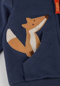 Marineblaues Sweatshirt mit einem Fuchs-Stickerei auf der Tasche. Verfügt über eine weiche Textur und gerippte Bündchen. Beinhaltet ein kräftig rotes Markenlabel.