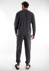 Graues Loungewear-Set bestehend aus einem Langarmoberteil und einer Hose, gefertigt aus weichem Stoff mit gerippten Bündchen und Bund, von hinten gezeigt.