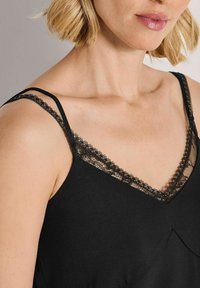 Zwarte cami-top met delicate kantafwerking langs de V-halslijn en verstelbare spaghetti-bandjes, gemaakt van een zachte, ademende stof.