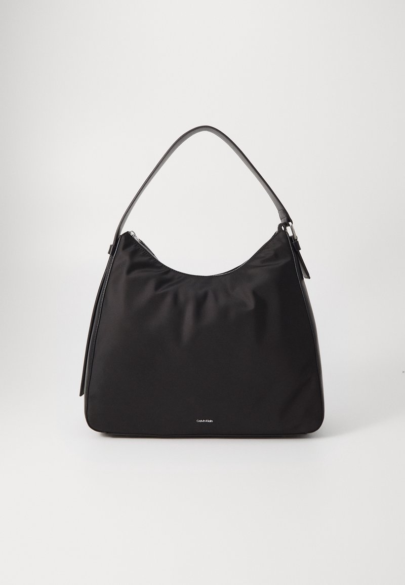 Sac à épaule noir Calvin Klein avec dessus courbé, bandoulière unique et logo discret à l'avant, présenté sur un fond clair uni.