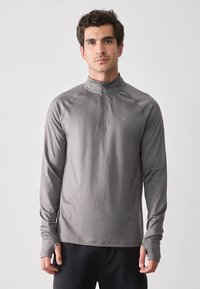 Camisola cinzenta de manga comprida, com gola de meio fecho de correr, textura macia, corte atlético e logótipo discreto no peito.