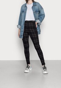 Jeansjacka i ljusblått, knäppt, lagd över en vit t-shirt och svarta rutiga högmidjade byxor. Chunkiga vita sneakers kompletterar outfiten.