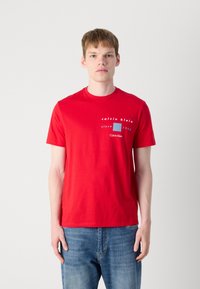 Punane puuvillane T-särk ümmarguse kaelusega, millel on ees valge ja sinine graafiline tekst "calvin klein since 1968".