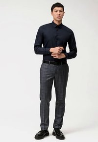 Marineblauw overhemd met knopen en kraag, gecombineerd met grijze geruite broek. Zwarte riem en glanzende zwarte schoenen maken de outfit compleet.