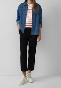 Veste en denim sur un tee-shirt à rayures rouges, associée à un pantalon noir cropped et des sneakers blanches. L'ensemble présente un look décontracté et superposé.