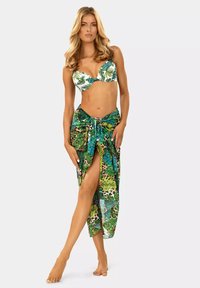 Bikini z tropikalnym wzorem liści w zielono-białych kolorach, w zestawie z długim, przezroczystym zielonym sarongiem, ozdobionym mieszanką nadruków roślinnych i związków.