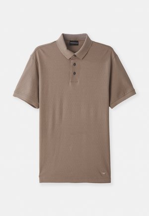 Brun polo skjorte med teksturert overflate, korte ermer, tre svarte knapper og en liten logo nederst til høyre.
