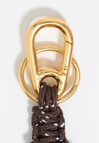 Gold metal clip with a round ring, attached to intertwined brown braided cord featuring white accents and engraved text.