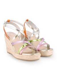 Sandalias de cuña metálica con tiras entrelazadas en plata, oro, rosa y verde. La suela de paja trenzada añade textura; incluye una correa ajustable en el tobillo.
