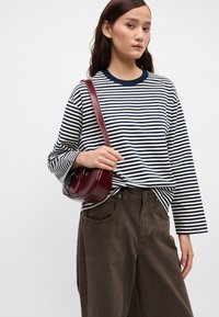 Τζιν πουκάμισο με ρίγες σε ναυτικό και κρεμ απόχρωση, συνδυασμένο με σκούρες καφέ παντελόνες με φαρδιά γραμμή. Μια μικρή μπορντό τσάντα χιαστί με επίπεδη λουρί.