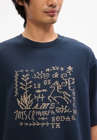 Ναυτι κό μπλε βαμβακερό μπλουζάκι με υφασματικό εκτύπωμα σε μπεζ, που περιλαμβάνει λουλουδάτα και ζωικά μοτίβα, όπως ένα άλογο και το έτος 1985.