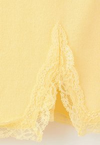 Tissu jaune tricoté avec détail de bordure en dentelle florale et bords festonnés sur l'ourlet d'un vêtement.