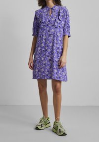 Floral purple dress with ruffled shoulders, keyhole neckline, short sleeves, and a loose fit; paired with green and black athletic sneakers.