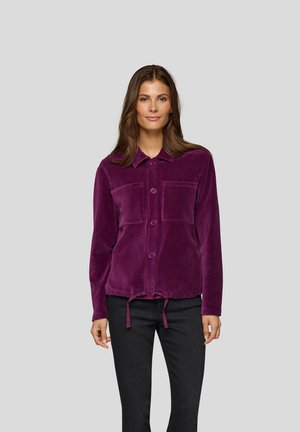 Purple corduroy button-up jacket with two chest pockets, drawstring hem, and long sleeves, worn over black pants. Smooth texture.