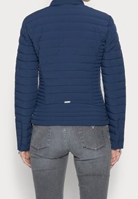 Giacca trapuntata blu navy con design aderente, colletto alto e maniche slim. Presenta cuciture orizzontali e un piccolo logo sul retro.