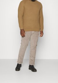 Brun ribbad tröja, beige kordbyxor, svarta läderankelboots. Enkel, figursydd design med en texturerad finish.