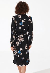 Černé květinové šaty s dlouhými rukávy, zdobené bílými a modrými květinovými vzory, s páskem v oblasti pasu a délka po kolena. Texturovaná tkanina.
