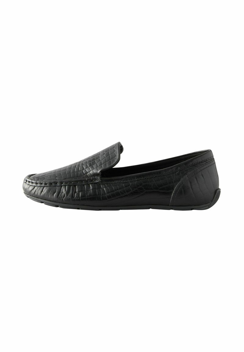 Mocasines de cuero negro con textura acolchada, diseño slip-on y suela de goma baja. Presentan una punta redondeada y detalles de costura mínimos.