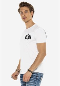 Weißes Baumwoll-T-Shirt mit kurzen Ärmeln, das auf der linken Brusttasche ein schwarzes Grafikmotiv "CB" und eine glatte, leichte Textur aufweist.