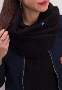 Black knitted infinity scarf with a textured pattern, worn over a fitted black top. It features visible stitching and a small logo detail.