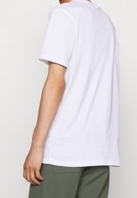 Bílé tričko z jemné bavlny, s krátkými rukávy a volným střihem. Jednoduchý design s klasickým kulatým výstřihem a bez loga či vzorů.