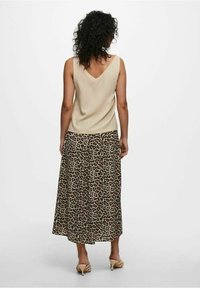 Top beige senza maniche con scollo a V, abbinato a una gonna leopardata di lunghezza media. Tessuto leggero con un design fluido e una texture morbida.