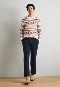 Vit stickad tröja med mönster i röd, grön och blå; marinblå byxor; ljusbruna ankelboots; mjuk textur och avslappnad passform.