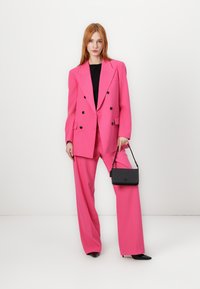 Double-breasted hot pink blazer and matching wide-leg trousers; paired with a black handbag and black pointed-toe shoes.