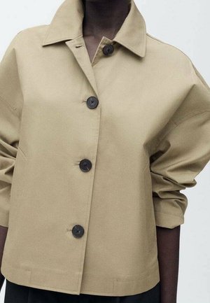 Beige button-up jacket with a wide collar, three dark buttons, and sleeves pushed up on dark-skinned person.
