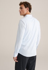 Világoskék, hosszúujjú ing standard gallérral, sima anyagból és gombos mandzsetta, sötét nadrággal párosítva. Tiszta dizájn, nincs minta.