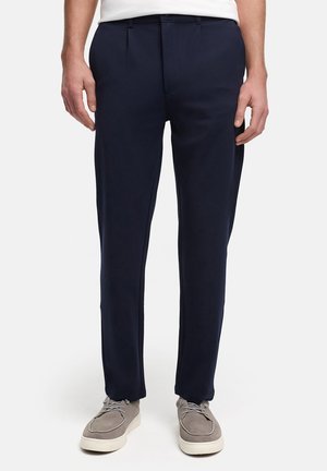 Pantalon bleu marine avec une texture lisse, présentant une coupe ajustée, deux plis à l'avant, des poches latérales et une ceinture à passants.