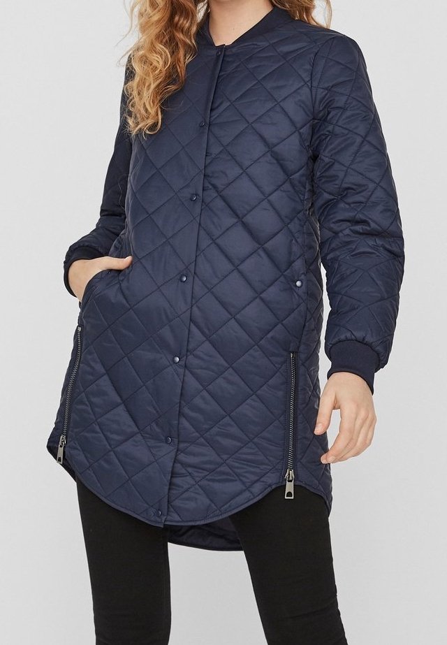 Marinblå quiltad lång jacka med tryckknappar, dragkedjefickor, ribbade muddar och rundad fåll. Tillverkad av lätt, isolerat material.