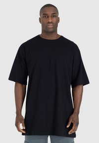 T-shirt in cotone nero con una vestibilità rilassata, maniche corte e scollo rotondo. Il tessuto appare liscio senza motivi o rifiniture visibili.