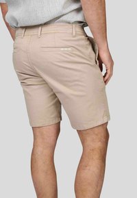 Shorts en coton beiges à coupe droite, dotés de deux poches arrière et d'une texture lisse. La ceinture comporte des passants de ceinture.