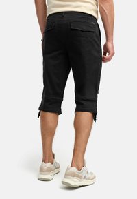 Svarte denimshorts med glidelås i kantene, midt på låret, med to baklommer og en glatt tekstur. Brukt sammen med lyse fargede sneakers.