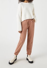 Krémový pletený svetr s širokými rukávy, kombinovaný s terrakotovými kalhotami rovného střihu a bílými kotníkovými botami s černou podešví. Jednoduchý design, texturovaná látka.