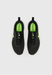 Sorte atletiske sko med en mesh-overdel, neongrønne detaljer og en hvid sål. Har en struktureret overflade og snøresystem.