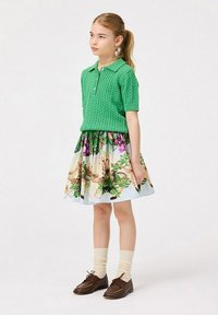 Grön kabelstickad polo skjorta i kombination med en blommig kjol med blad och blommor. Bruna snörskor och krämfärgade strumpor.