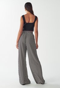 Cropped black tank top paired with wide, patterned trousers in black and beige diamond shapes, featuring a relaxed fit and elastic waistband.