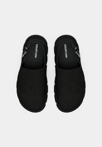 Czarne buty wsuwane o eleganckim designie, z gładką górną częścią, teksturowaną podeszwą i logo na wkładce.